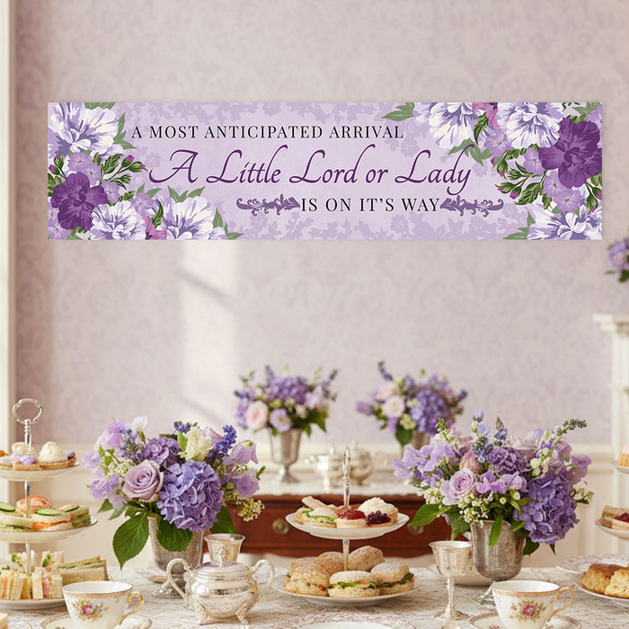 Baby shower banner with floral design and text above a table set with tea cups and sandwiches.