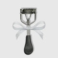 Silver eyelash curler with a white glittery ribbon bow tied around the center.