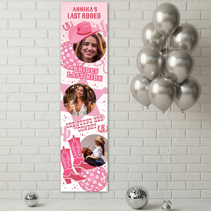 A vertical pink and white custom party banner displayed on a white brick wall, featuring customizable photos of a woman, cowboy boots, a cowboy hat, and a disco ball with text reading 'Annika's Last Rodeo', 'Bride's Last Rodeo', and 'She Found Her Cowboy'. Silver balloons and disco balls decorate the scene.
