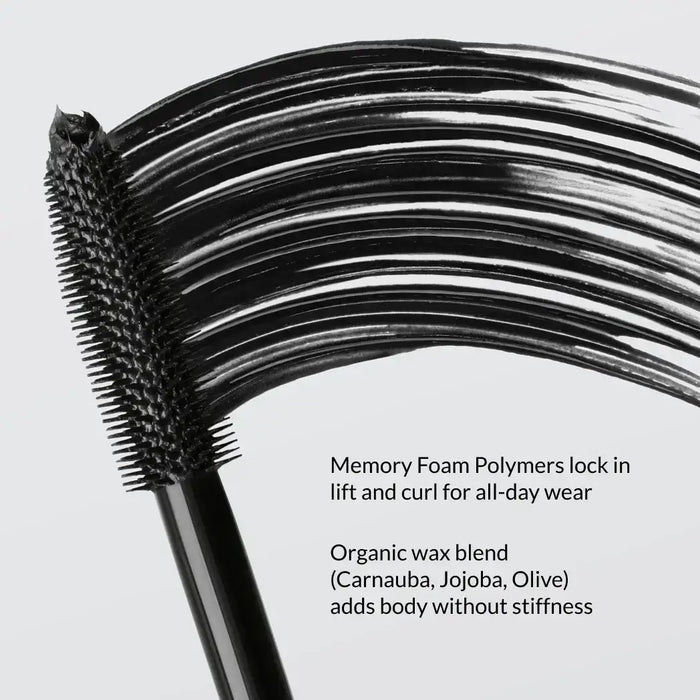 Mascara wand applying glossy black formula to long, curled lashes.